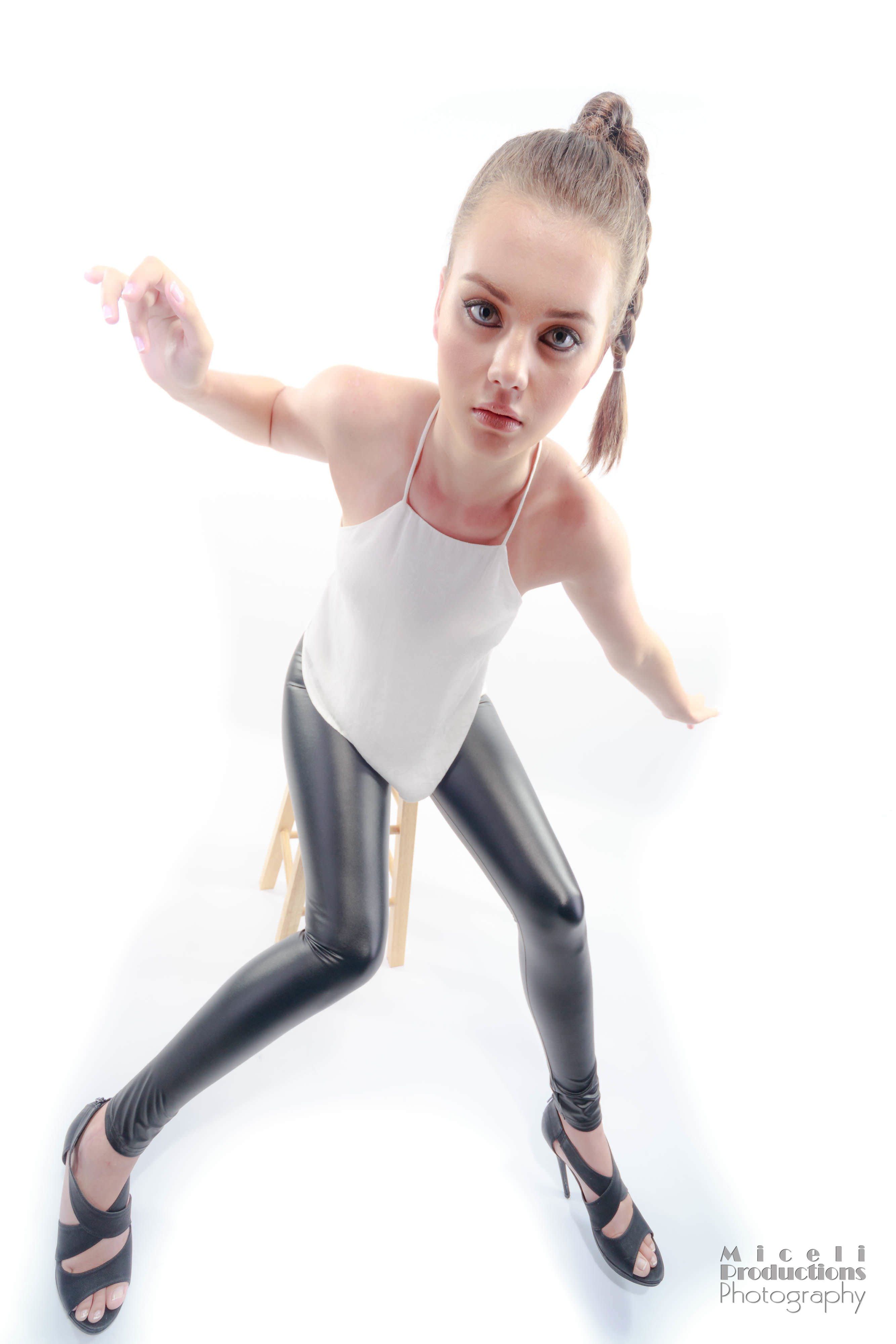Girl model with a white tank top and black pleather pants walking strangely towards camera, looking like a doll with an effect that makes her head seem larger than her body.