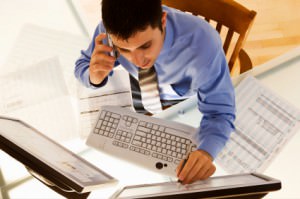 Photo of a man on the phone at a keyboard at his desk. Image from iStockPhoto