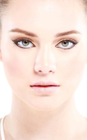 A face portrait of a model with striking makeup on a white background for a fashion photo shoot.