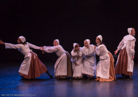 Several woman in early American clothes performing for Thw Witching Hour, at left one if pulling another by the arm to prevent her from going off