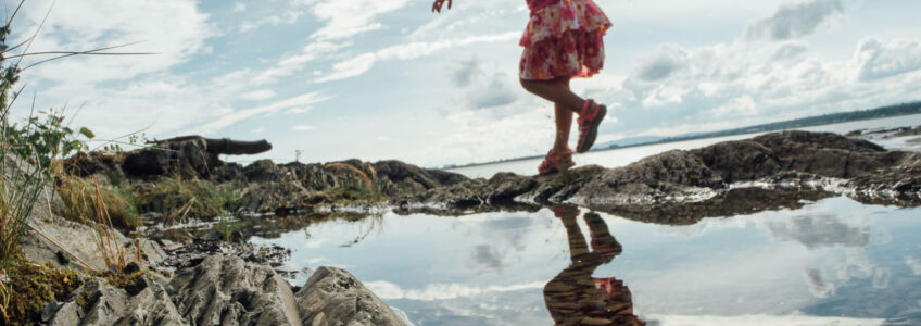 Young girl runs through the tide pools near the beach with the open blue sky above her.