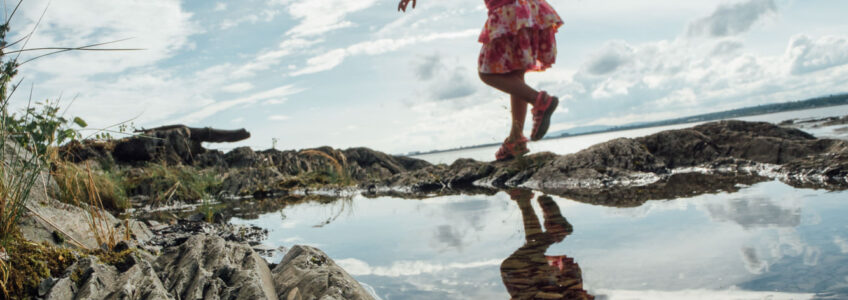 Young girl runs through the tide pools near the beach with the open blue sky above her. {{brizy_dc_image_alt entityId=