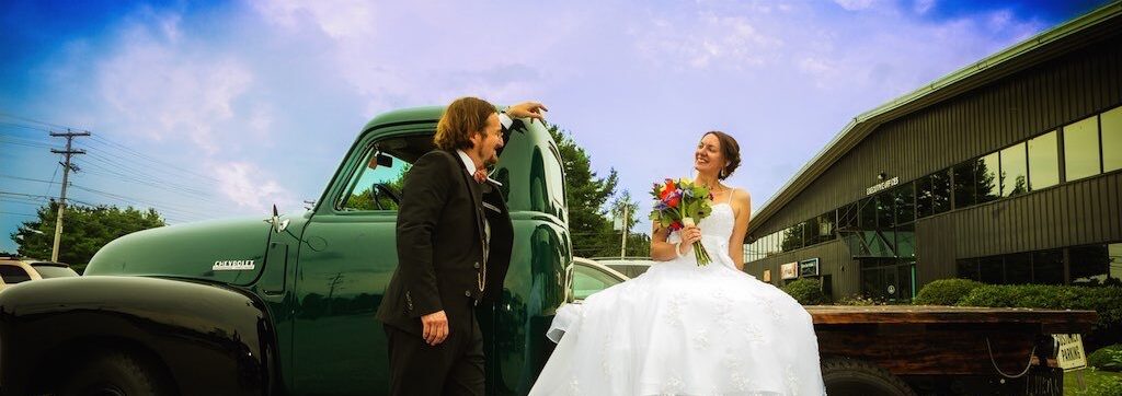 Bride and groom couple sitting on an old Ford pick-up truck with a bright blue sky on their wedding day.